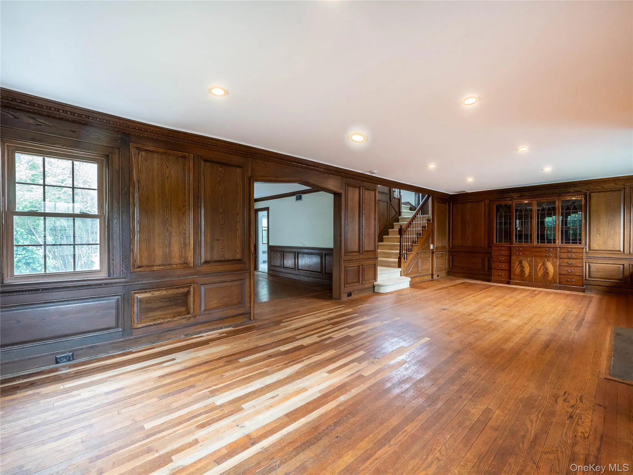 Unfurnished living room featuring wood walls, light wood finished floors, a decorative wall, ornamental molding, and recessed lighting Unfurnished living room featuring wood walls, light wood finished floors, a decorative wall, ornamental molding, and recessed lighting