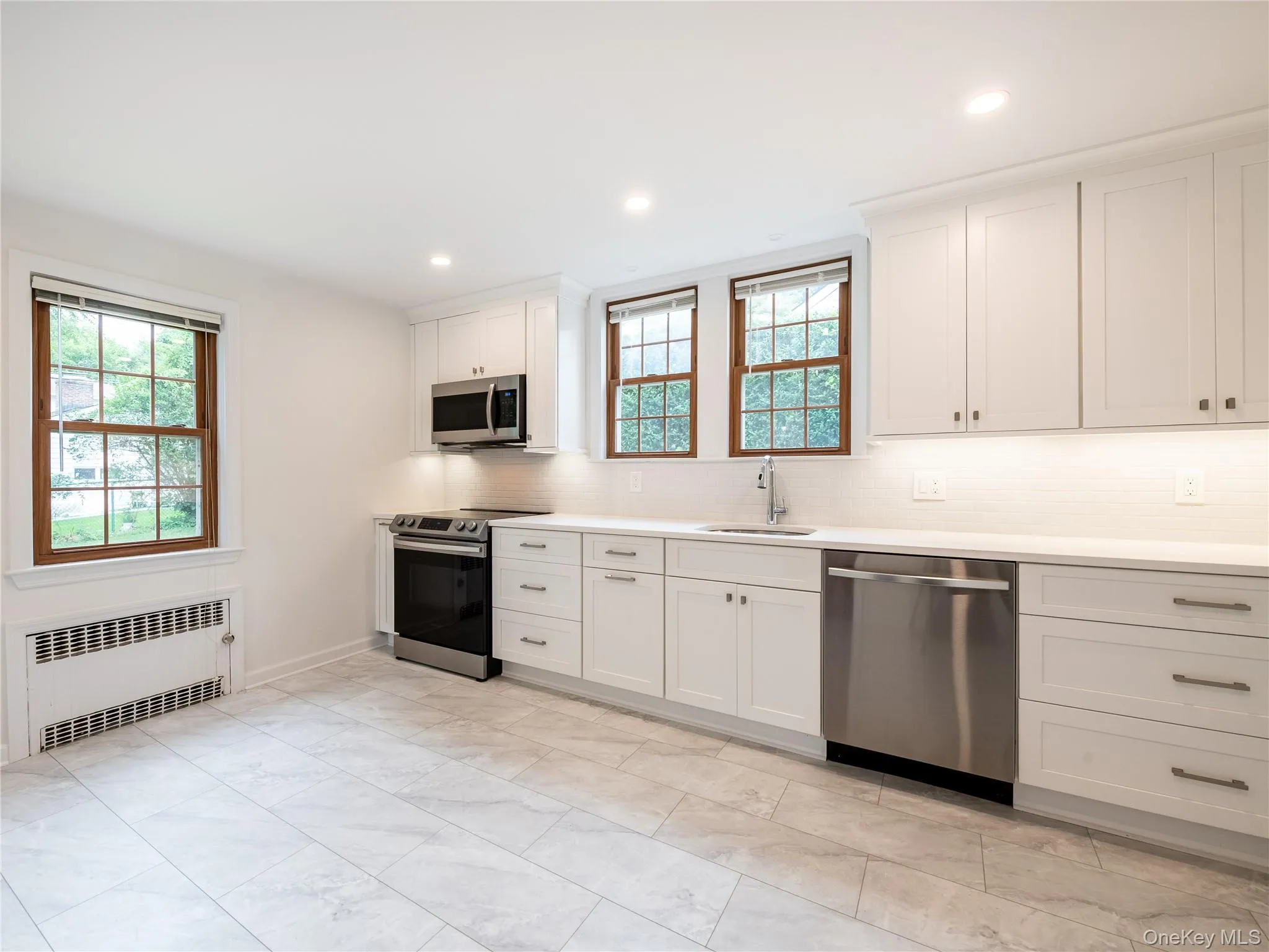 Kitchen with backsplash, appliances with stainless steel finishes, radiator heating unit, white cabinets, and recessed lighting Kitchen with backsplash, appliances with stainless steel finishes, radiator heating unit, white cabinets, and recessed lighting