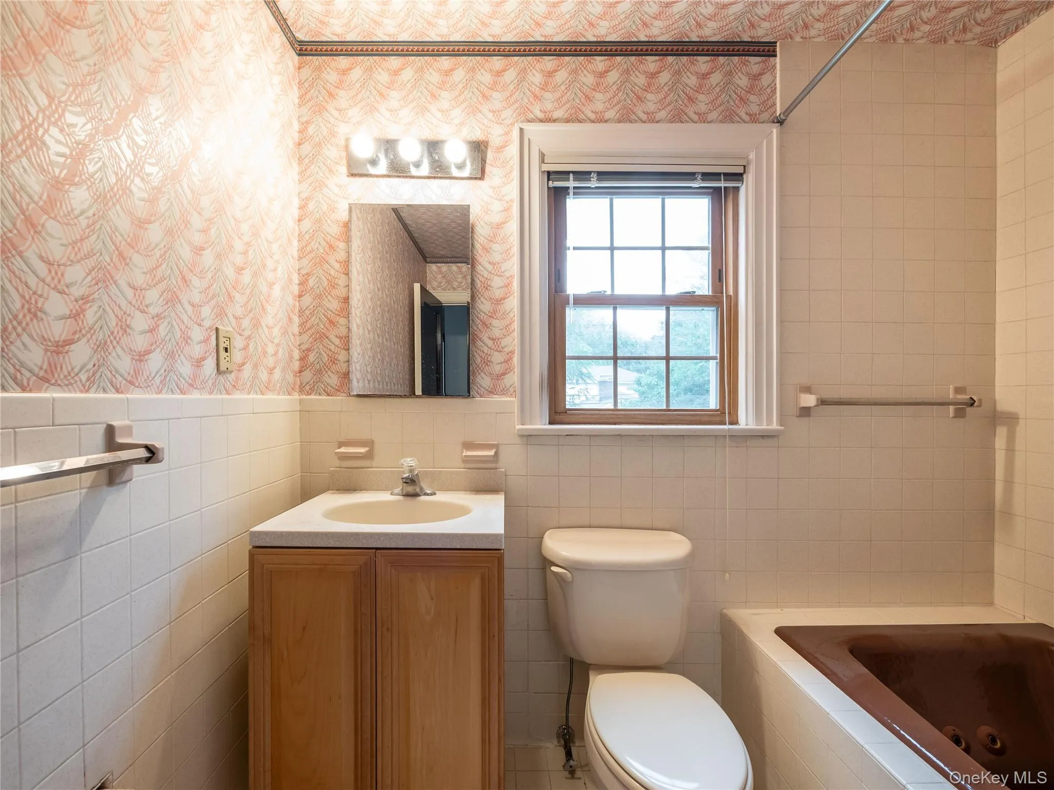Full bath featuring wallpapered walls, vanity, a tub with jets, and tile walls Full bath featuring wallpapered walls, vanity, a tub with jets, and tile walls