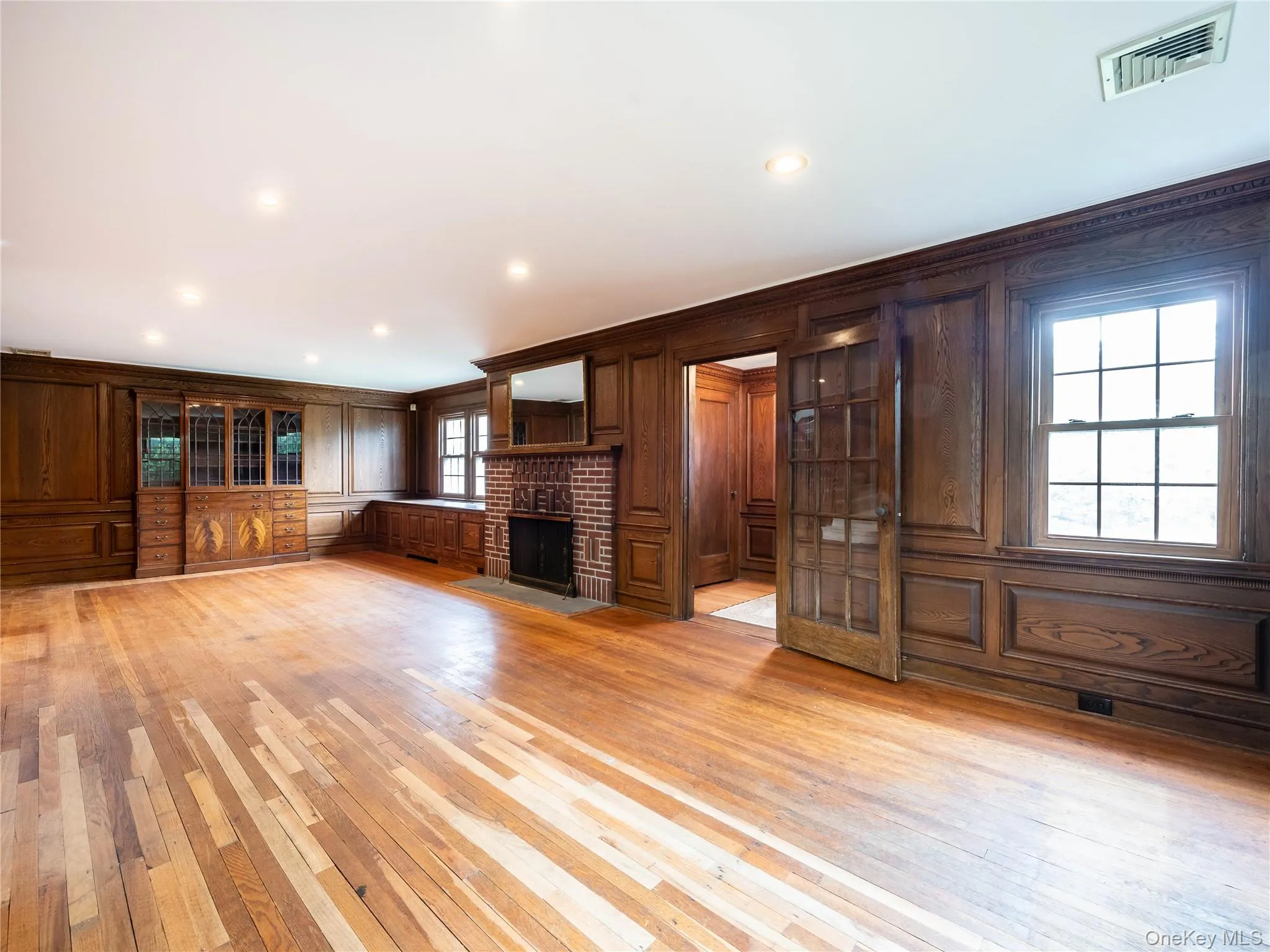 Unfurnished living room featuring light wood-style floors, a brick fireplace, recessed lighting, wooden walls, and crown molding Unfurnished living room featuring light wood-style floors, a brick fireplace, recessed lighting, wooden walls, and crown molding