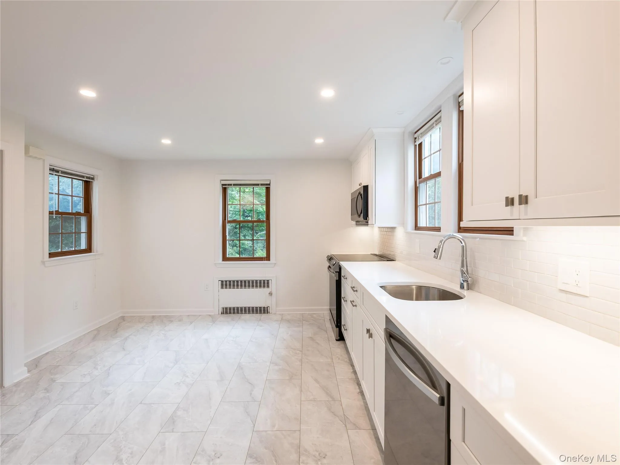 Kitchen with white cabinetry, appliances with stainless steel finishes, light stone countertops, backsplash, and recessed lighting Kitchen with white cabinetry, appliances with stainless steel finishes, light stone countertops, backsplash, and recessed lighting