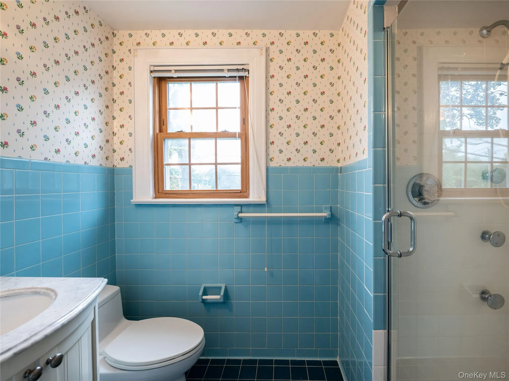 Bathroom with tile walls, a shower stall, a wainscoted wall, vanity, and dark tile patterned flooring Bathroom with tile walls, a shower stall, a wainscoted wall, vanity, and dark tile patterned flooring