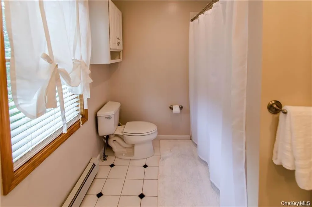 Bathroom with a baseboard heating unit, light tile patterned flooring, and a shower with shower curtain Bathroom with a baseboard heating unit, light tile patterned flooring, and a shower with shower curtain