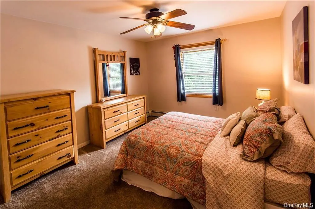 Bedroom featuring dark colored carpet, ceiling fan, and a baseboard heating unit Bedroom featuring dark colored carpet, ceiling fan, and a baseboard heating unit