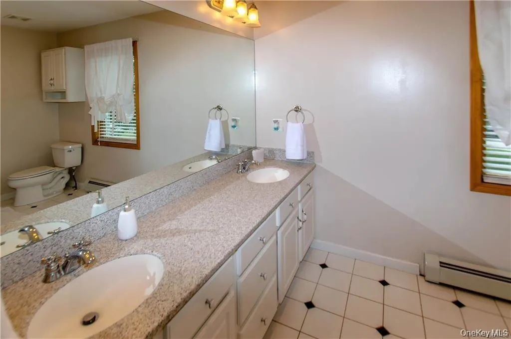 Bathroom with double vanity, light tile patterned floors, and a baseboard radiator Bathroom with double vanity, light tile patterned floors, and a baseboard radiator
