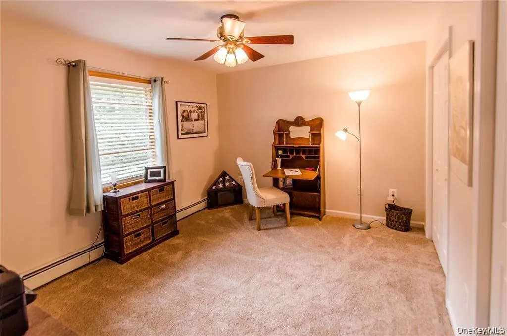 Living area featuring a baseboard heating unit, light colored carpet, and ceiling fan Living area featuring a baseboard heating unit, light colored carpet, and ceiling fan