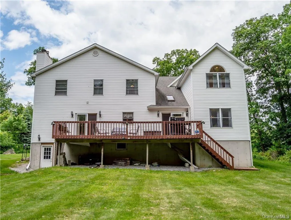 Back of house featuring a wooden deck, stairs, a lawn, and a chimney Back of house featuring a wooden deck, stairs, a lawn, and a chimney