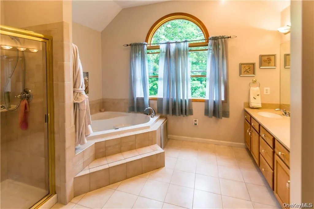 Bathroom with a bath, a stall shower, light tile patterned floors, vanity, and vaulted ceiling Bathroom with a bath, a stall shower, light tile patterned floors, vanity, and vaulted ceiling