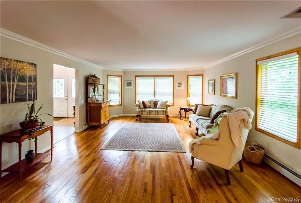 Living area with ornamental molding, wood finished floors, healthy amount of natural light, and baseboard heating Living area with ornamental molding, wood finished floors, healthy amount of natural light, and baseboard heating
