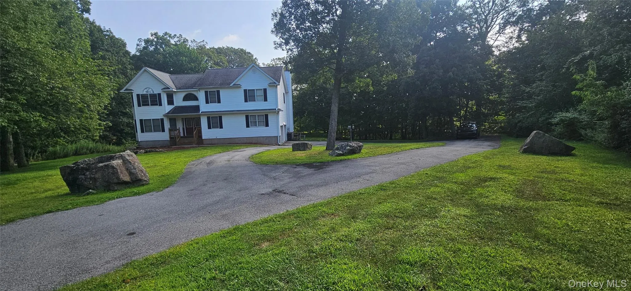 View of front of house with a front yard, asphalt driveway, and view of wooded area View of front of house with a front yard, asphalt driveway, and view of wooded area