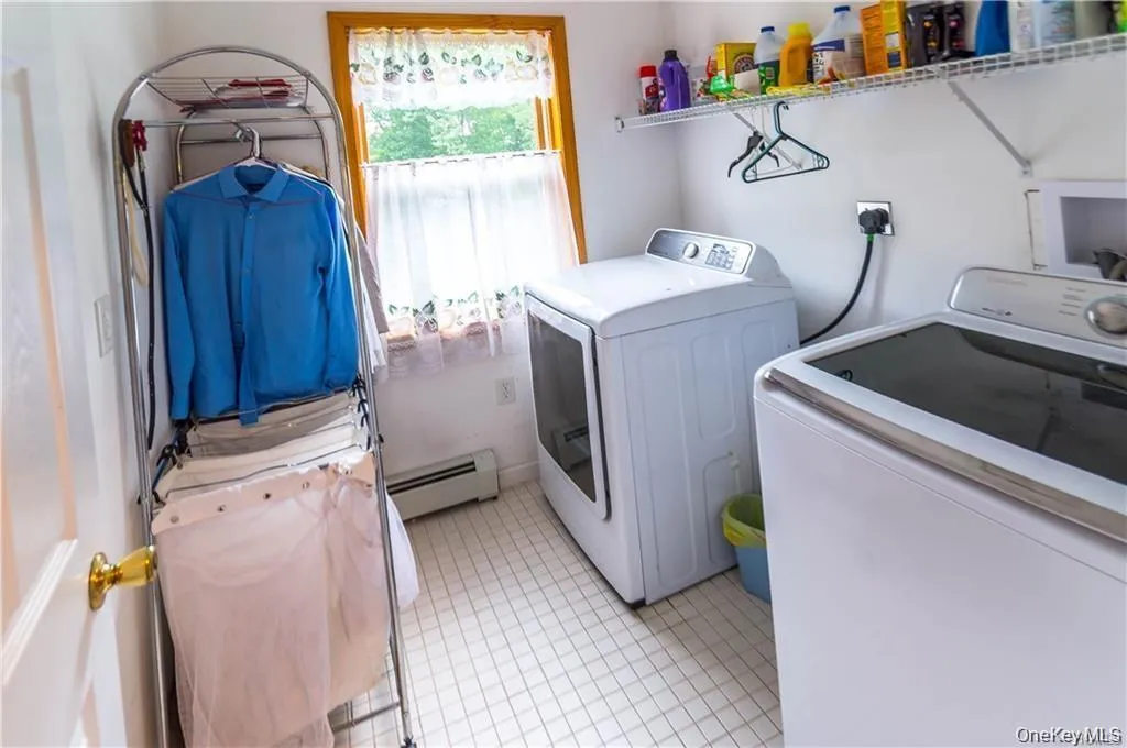 Laundry room featuring light tile patterned flooring, washing machine and clothes dryer, and a baseboard radiator Laundry room featuring light tile patterned flooring, washing machine and clothes dryer, and a baseboard radiator