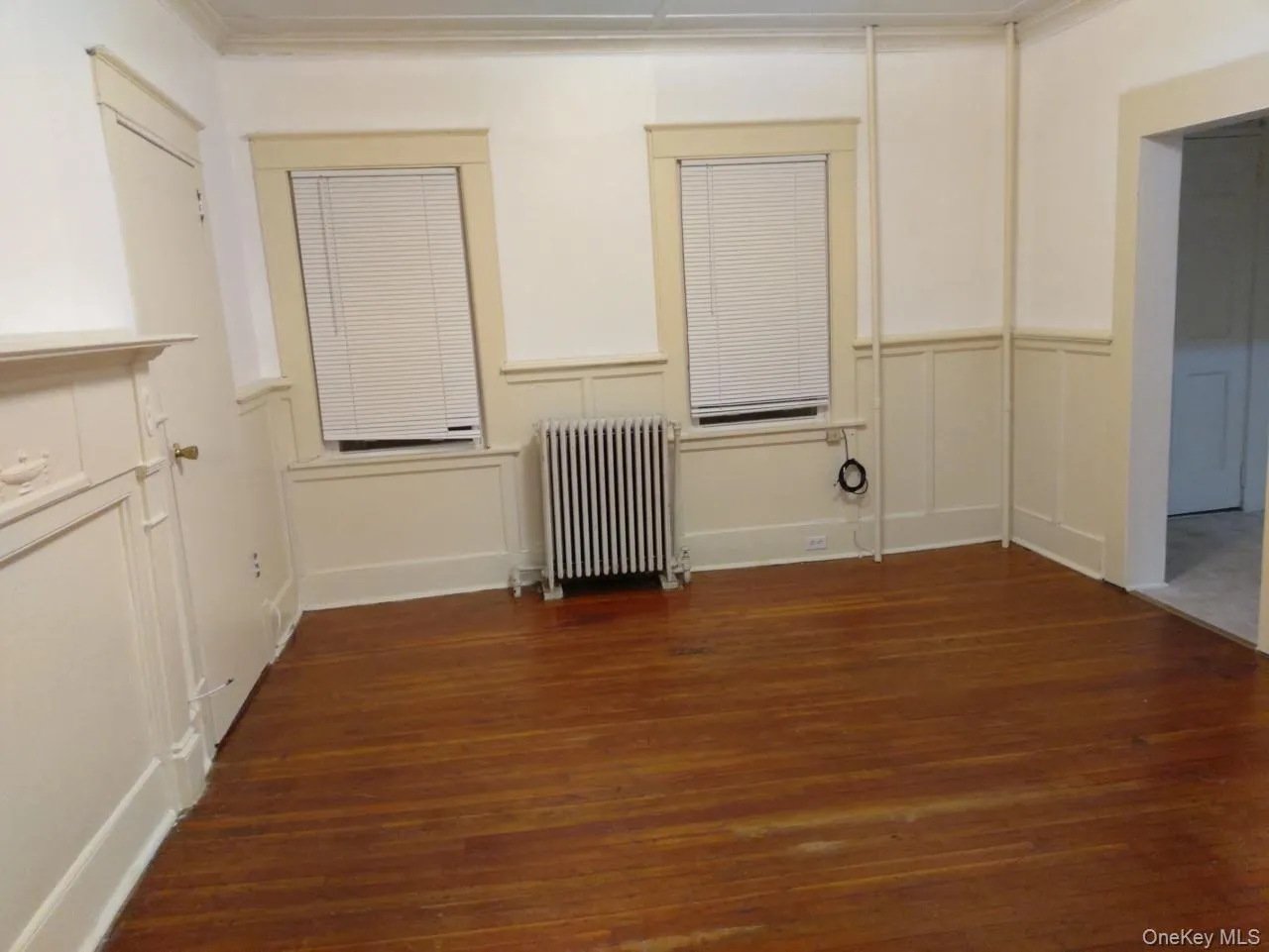 Empty room with a decorative wall, radiator, dark wood-type flooring, a wainscoted wall, and ornamental molding Empty room with a decorative wall, radiator, dark wood-type flooring, a wainscoted wall, and ornamental molding
