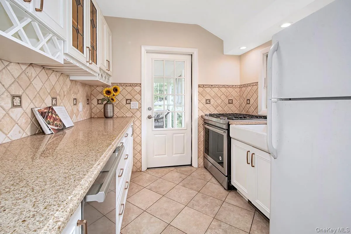 Kitchen featuring stainless steel appliances, white cabinets, light tile patterned flooring, glass insert cabinets, and light stone counters Kitchen featuring stainless steel appliances, white cabinets, light tile patterned flooring, glass insert cabinets, and light stone counters