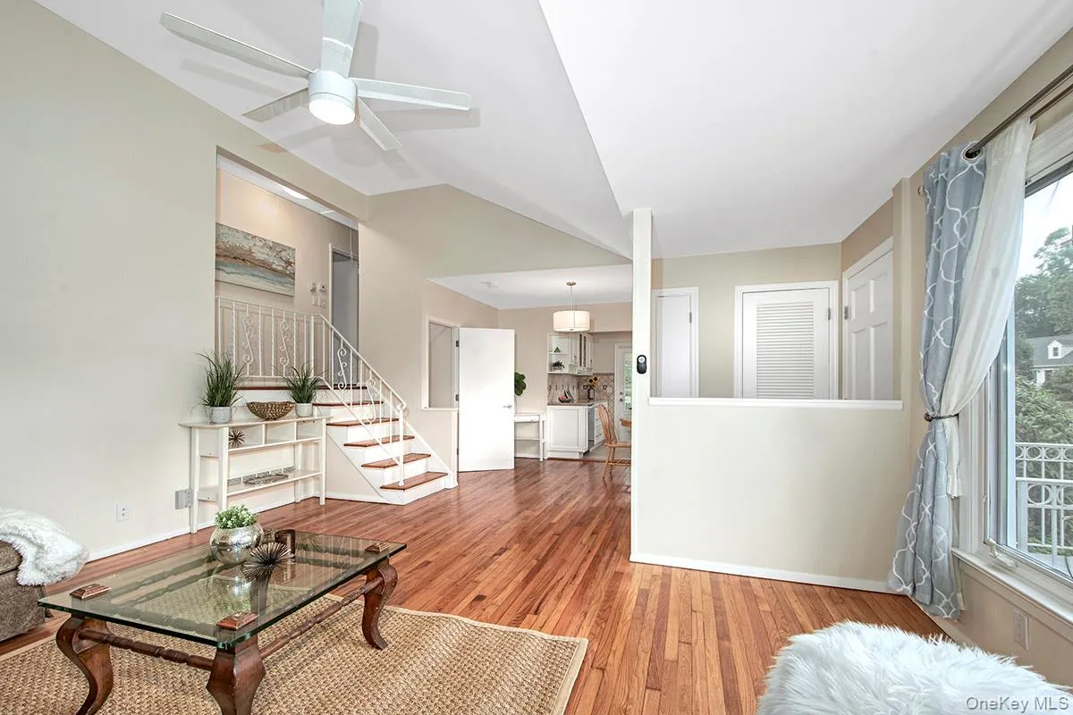 Living room with stairs, wood finished floors, vaulted ceiling, and ceiling fan Living room with stairs, wood finished floors, vaulted ceiling, and ceiling fan