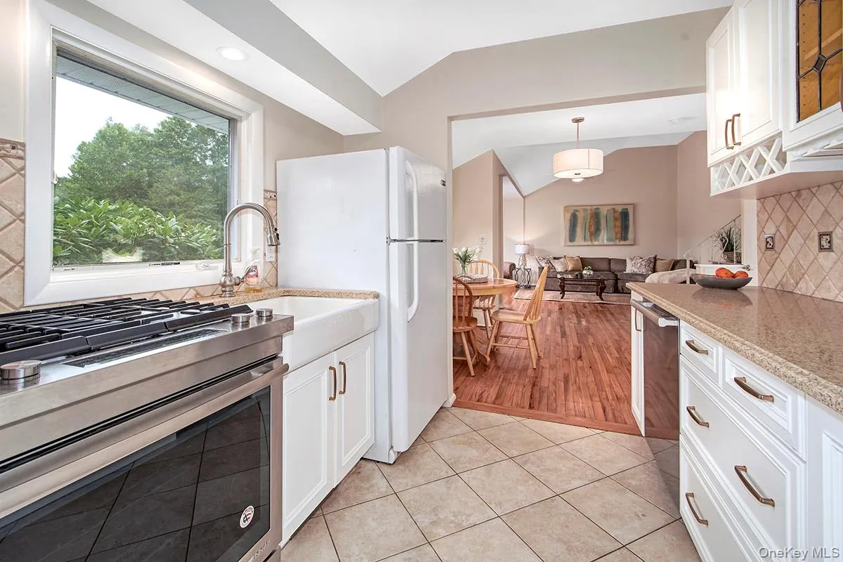 Kitchen with backsplash, appliances with stainless steel finishes, white cabinets, vaulted ceiling, and light tile patterned floors Kitchen with backsplash, appliances with stainless steel finishes, white cabinets, vaulted ceiling, and light tile patterned floors