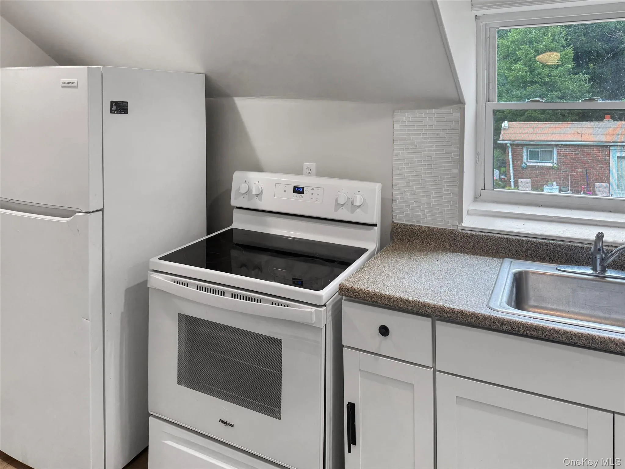Kitchen featuring white appliances, dark countertops, and white cabinetry Kitchen featuring white appliances, dark countertops, and white cabinetry