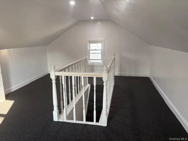 Additional living space featuring vaulted ceiling and dark colored carpet Additional living space featuring vaulted ceiling and dark colored carpet