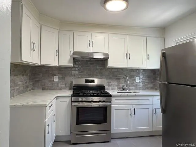 Kitchen featuring stainless steel appliances, white cabinetry, light stone counters, and under cabinet range hood Kitchen featuring stainless steel appliances, white cabinetry, light stone counters, and under cabinet range hood