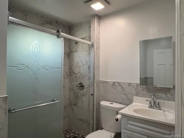 Bathroom featuring vanity, a shower stall, and tile walls Bathroom featuring vanity, a shower stall, and tile walls