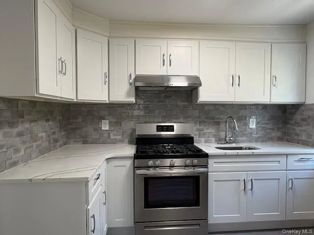 Kitchen with gas range, white cabinetry, light stone counters, tasteful backsplash, and under cabinet range hood Kitchen with gas range, white cabinetry, light stone counters, tasteful backsplash, and under cabinet range hood