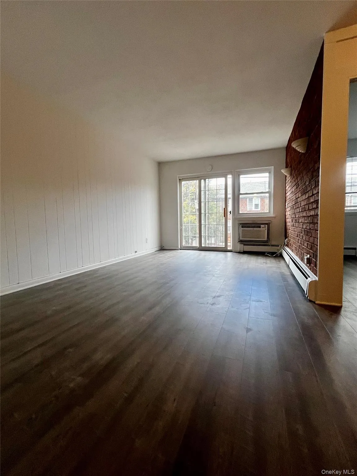 Unfurnished living room featuring dark wood-type flooring, a wall mounted AC, and a baseboard radiator Unfurnished living room featuring dark wood-type flooring, a wall mounted AC, and a baseboard radiator