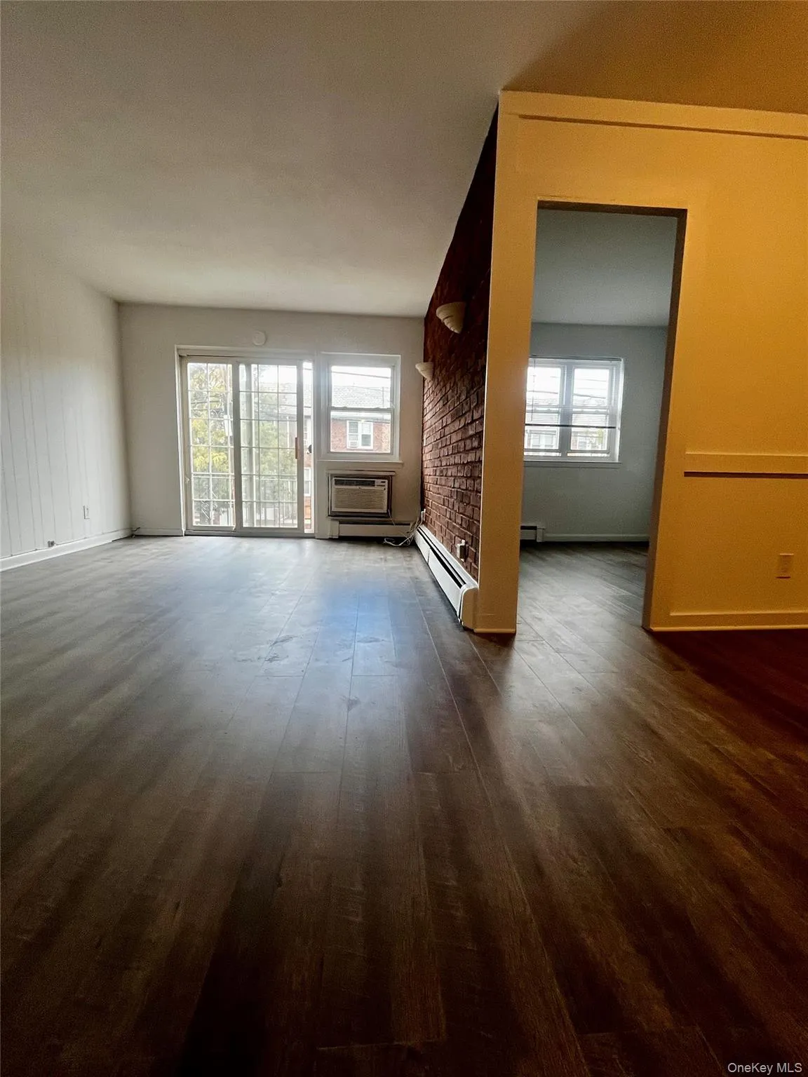 Unfurnished living room with dark wood finished floors, a wall mounted air conditioner, and a baseboard radiator Unfurnished living room with dark wood finished floors, a wall mounted air conditioner, and a baseboard radiator
