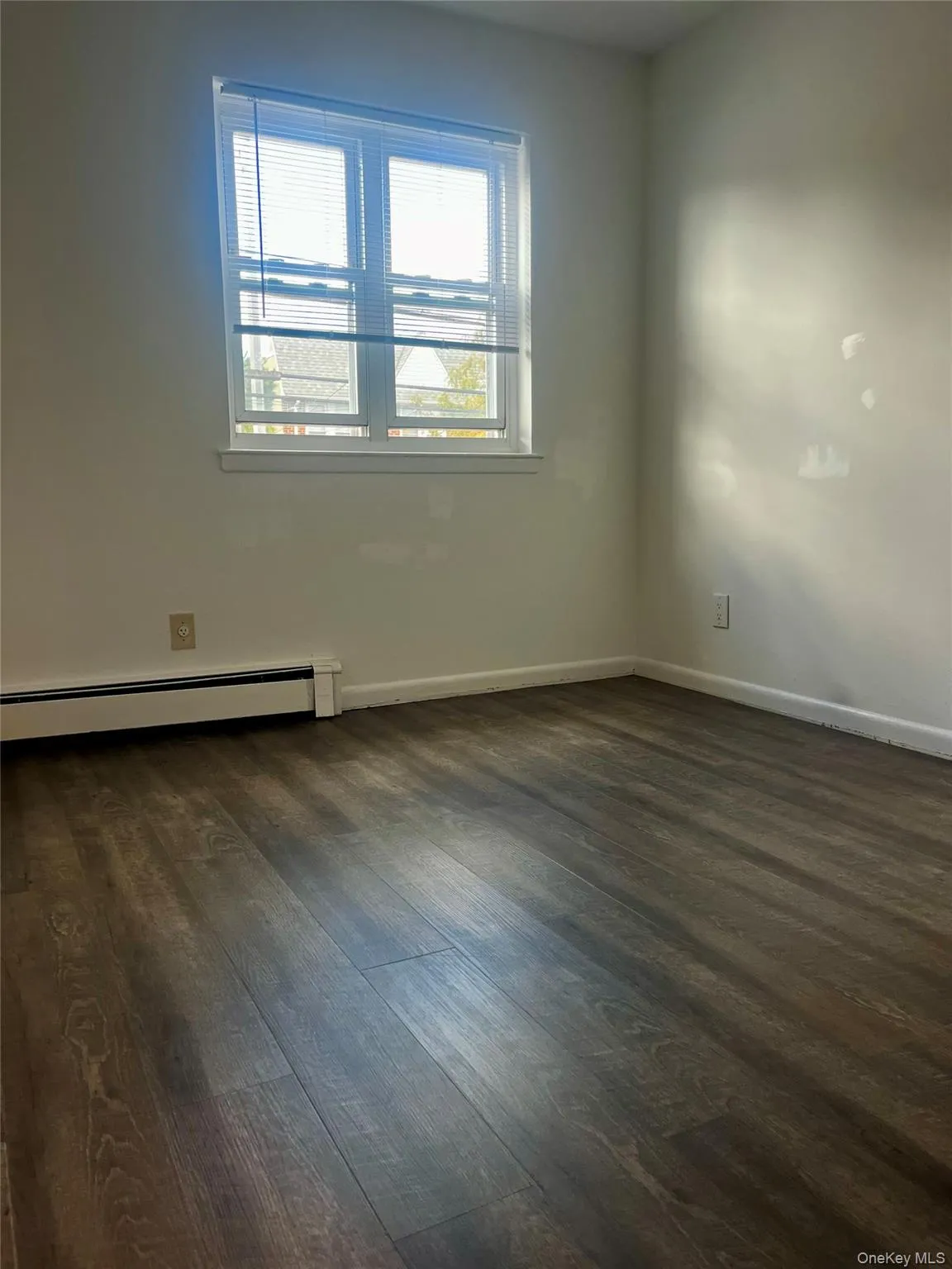 Unfurnished room with baseboard heating and dark wood-type flooring Unfurnished room with baseboard heating and dark wood-type flooring