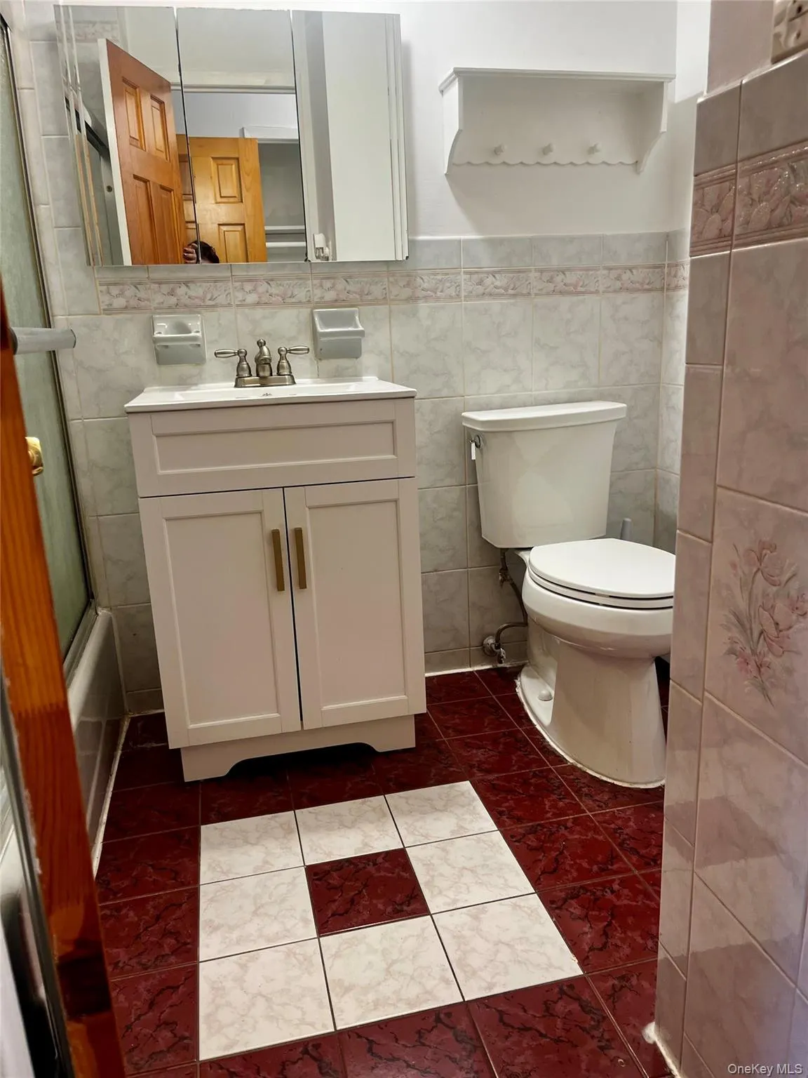 Full bathroom featuring tile walls, enclosed tub / shower combo, vanity, dark tile patterned floors, and wainscoting Full bathroom featuring tile walls, enclosed tub / shower combo, vanity, dark tile patterned floors, and wainscoting