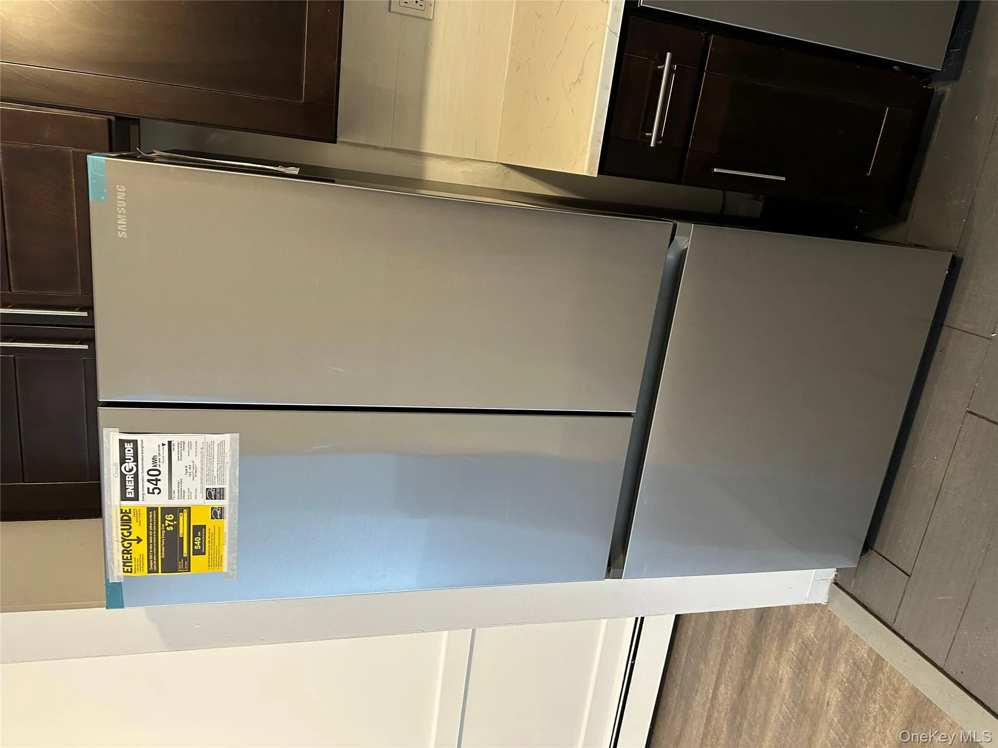 Kitchen view of dark brown cabinets, freestanding refrigerator, a baseboard radiator, and light stone countertops Kitchen view of dark brown cabinets, freestanding refrigerator, a baseboard radiator, and light stone countertops