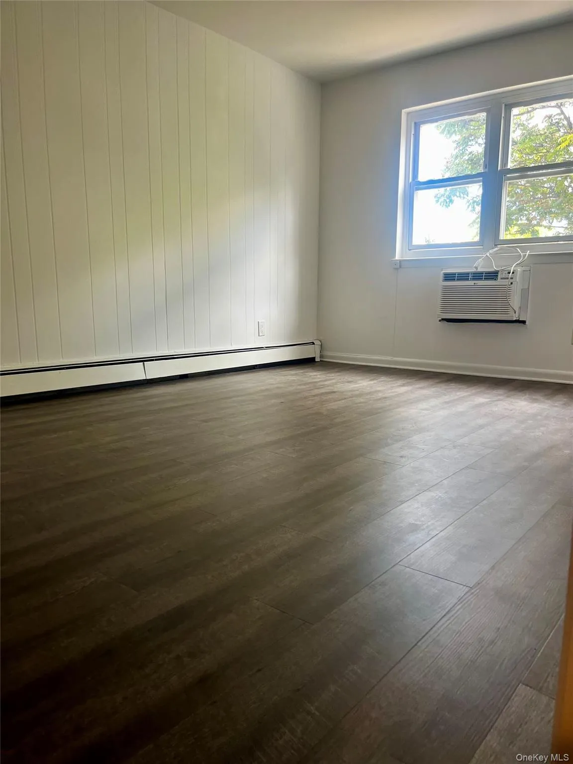 Empty room featuring dark wood-style floors, a baseboard heating unit, and a wall unit AC Empty room featuring dark wood-style floors, a baseboard heating unit, and a wall unit AC