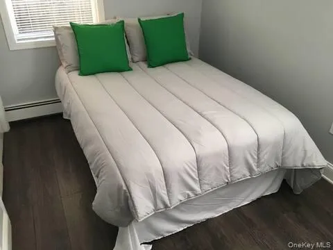 Bedroom with dark wood finished floors and a baseboard heating unit Bedroom with dark wood finished floors and a baseboard heating unit