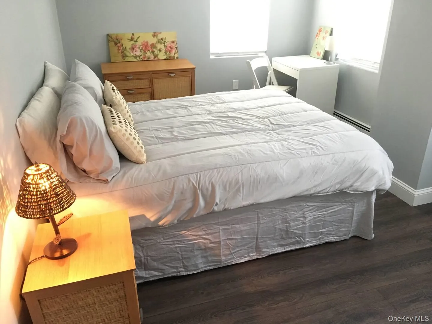 Bedroom featuring dark wood-style flooring, a baseboard radiator, and multiple windows Bedroom featuring dark wood-style flooring, a baseboard radiator, and multiple windows