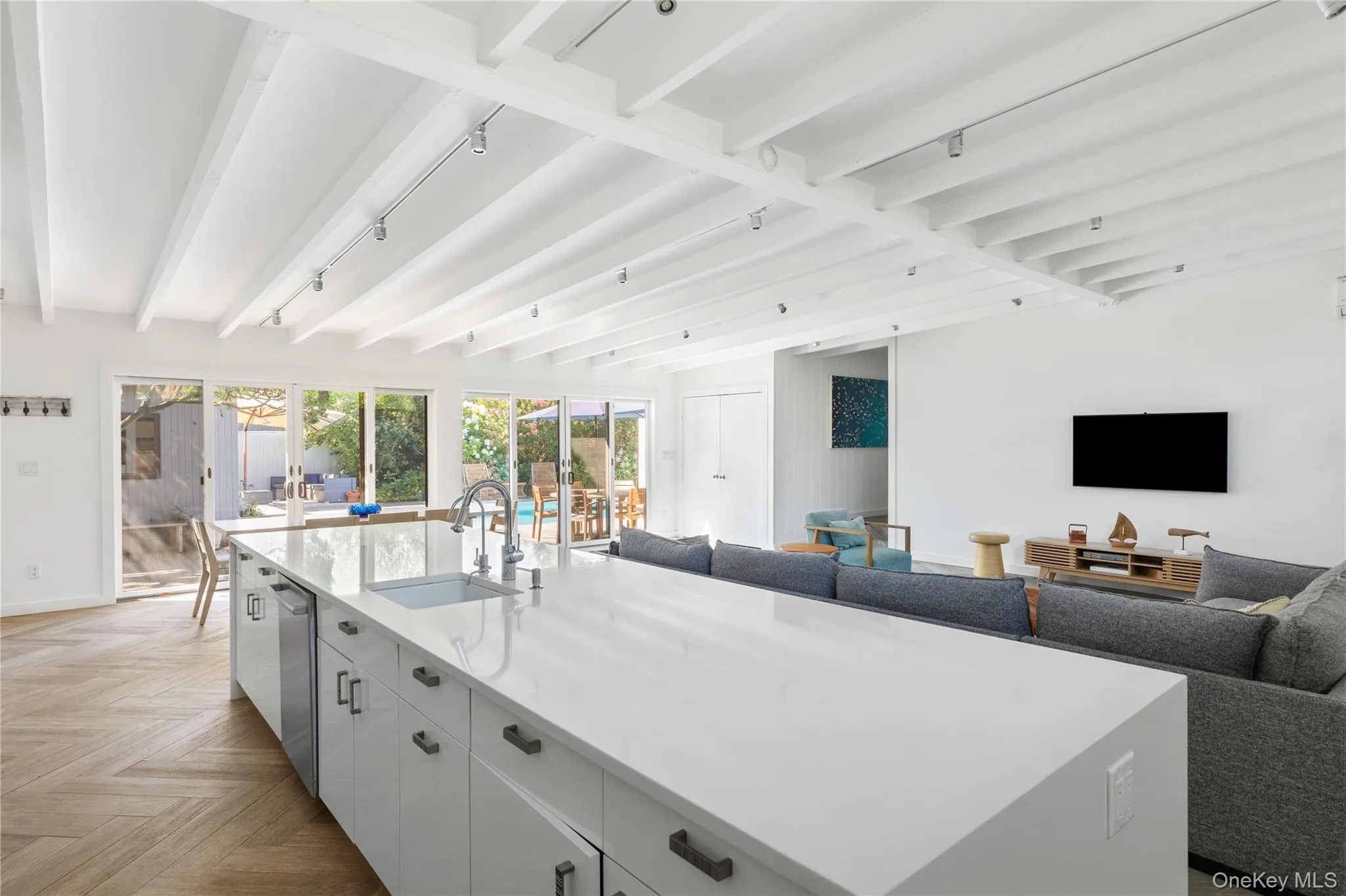 Kitchen with open floor plan, white cabinetry, beam ceiling, a spacious island, and light stone countertops Kitchen with open floor plan, white cabinetry, beam ceiling, a spacious island, and light stone countertops