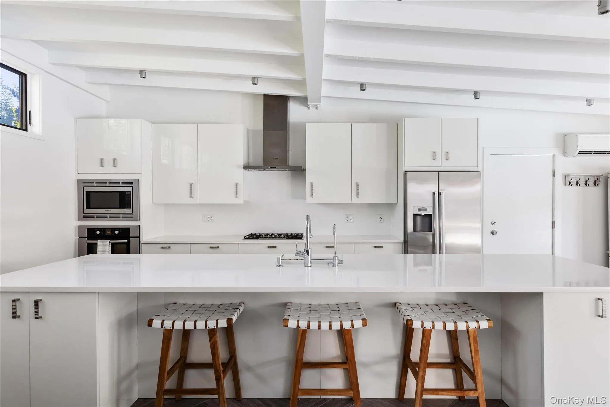 Kitchen with white cabinetry, a large island with sink, a breakfast bar area, stainless steel appliances, and beam ceiling Kitchen with white cabinetry, a large island with sink, a breakfast bar area, stainless steel appliances, and beam ceiling