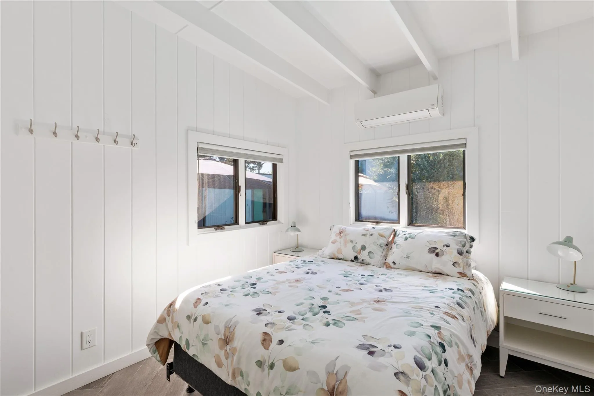 Bedroom with multiple windows, an AC wall unit, beamed ceiling, and wooden walls Bedroom with multiple windows, an AC wall unit, beamed ceiling, and wooden walls