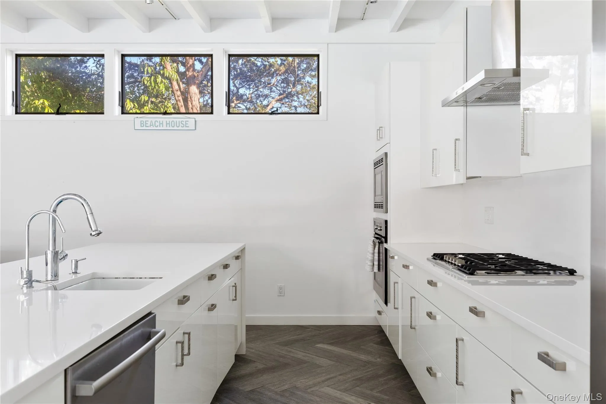 Kitchen featuring white cabinetry, wall chimney range hood, appliances with stainless steel finishes, beam ceiling, and modern cabinets Kitchen featuring white cabinetry, wall chimney range hood, appliances with stainless steel finishes, beam ceiling, and modern cabinets