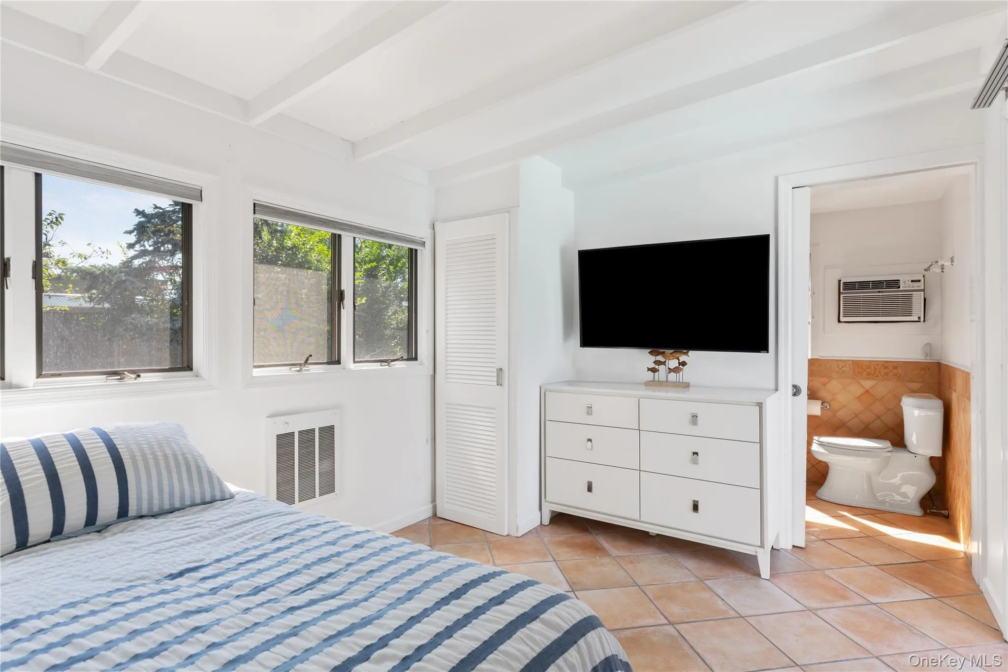 Bedroom featuring light tile patterned floors, beam ceiling, heating unit, and a wall unit AC Bedroom featuring light tile patterned floors, beam ceiling, heating unit, and a wall unit AC