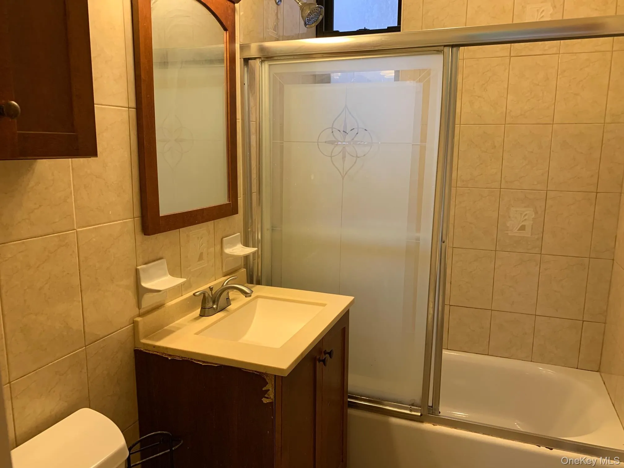 Full bathroom featuring vanity, tile walls, and shower / bath combination with glass door Full bathroom featuring vanity, tile walls, and shower / bath combination with glass door