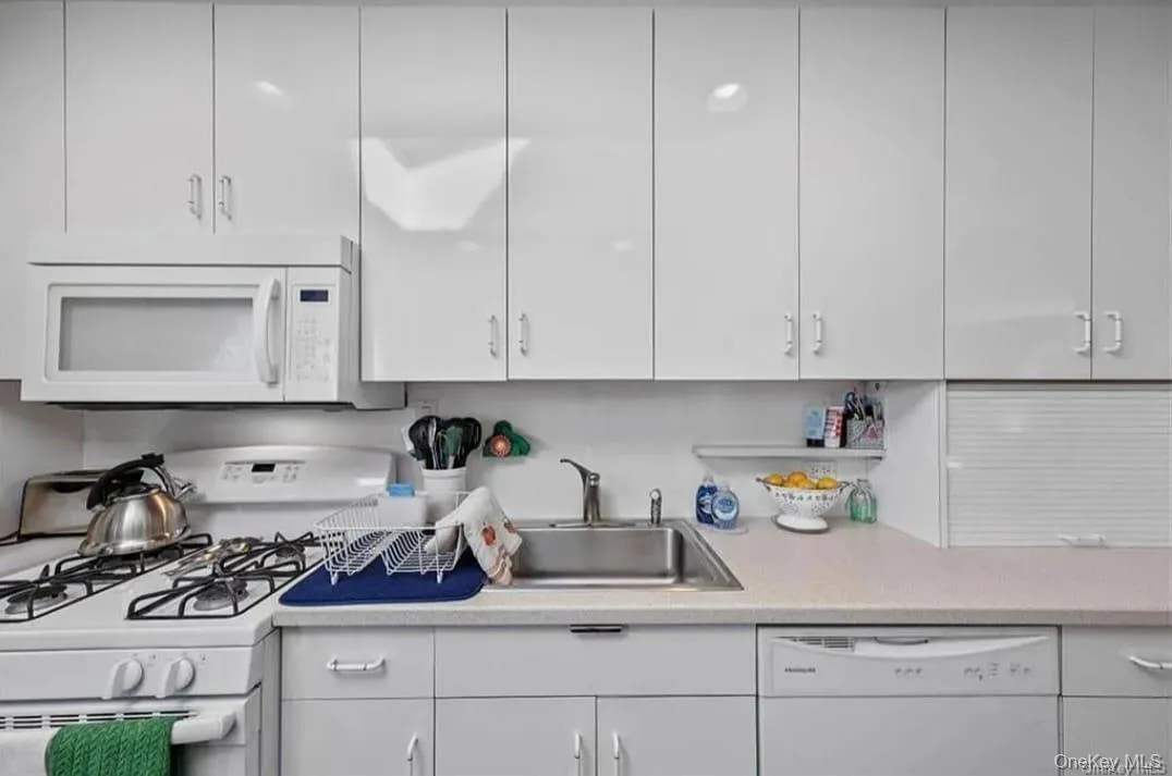 Kitchen featuring white appliances, light countertops, and white cabinetry Kitchen featuring white appliances, light countertops, and white cabinetry