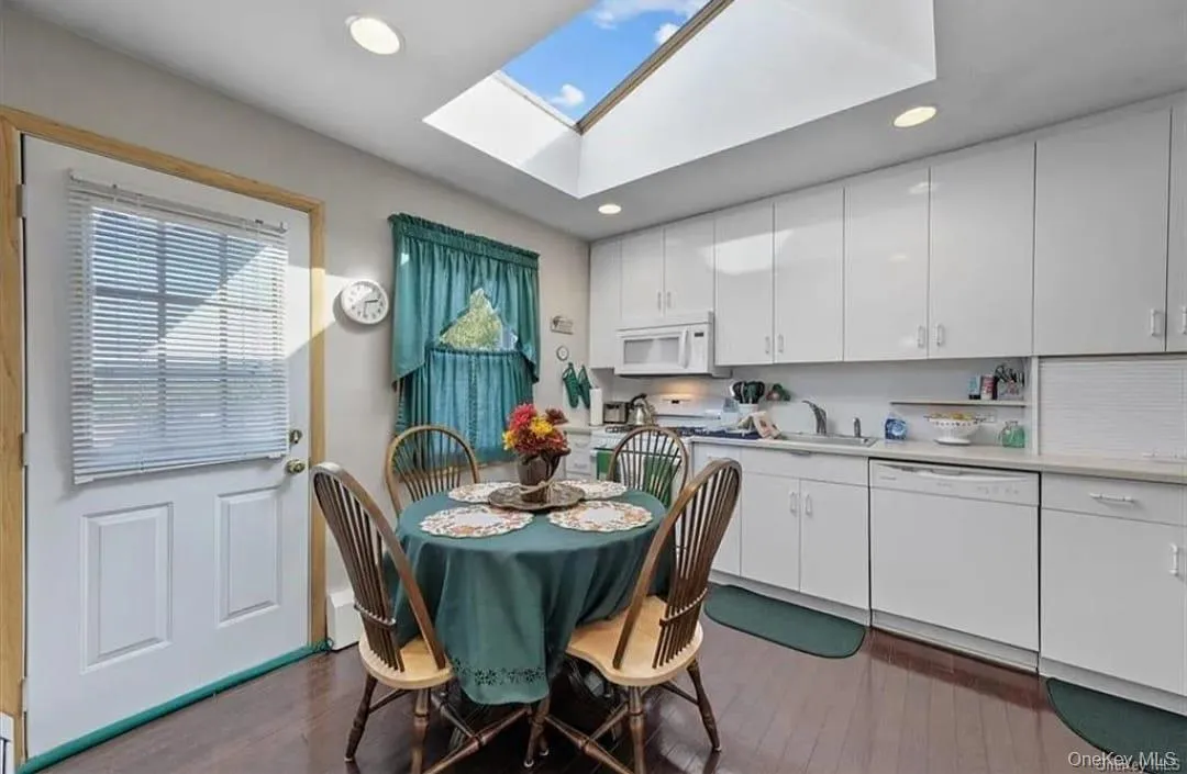 Kitchen with white cabinetry, light countertops, white appliances, dark wood-type flooring, and a skylight Kitchen with white cabinetry, light countertops, white appliances, dark wood-type flooring, and a skylight