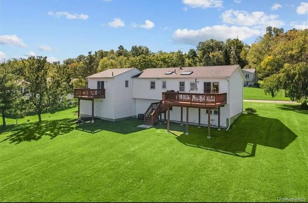 Back of property with a wooden deck, a lawn, and stairway Back of property with a wooden deck, a lawn, and stairway
