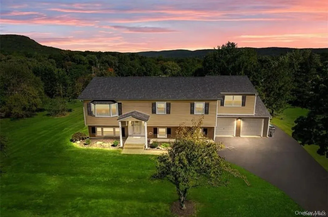 Bi-level home featuring a front lawn, an attached garage, driveway, and a forest view Bi-level home featuring a front lawn, an attached garage, driveway, and a forest view