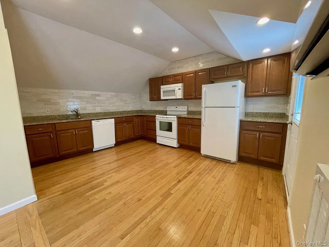 Kitchen with tasteful backsplash, lofted ceiling, white appliances, light wood-type flooring, and light stone countertops Kitchen with tasteful backsplash, lofted ceiling, white appliances, light wood-type flooring, and light stone countertops