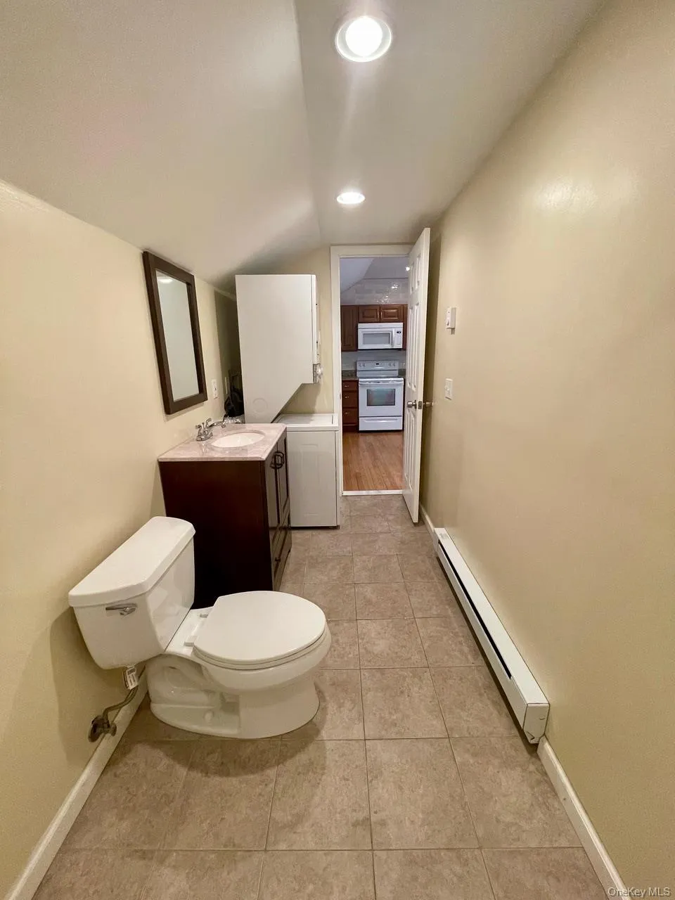 Half bathroom featuring a baseboard heating unit, vanity, light tile patterned floors, and lofted ceiling Half bathroom featuring a baseboard heating unit, vanity, light tile patterned floors, and lofted ceiling