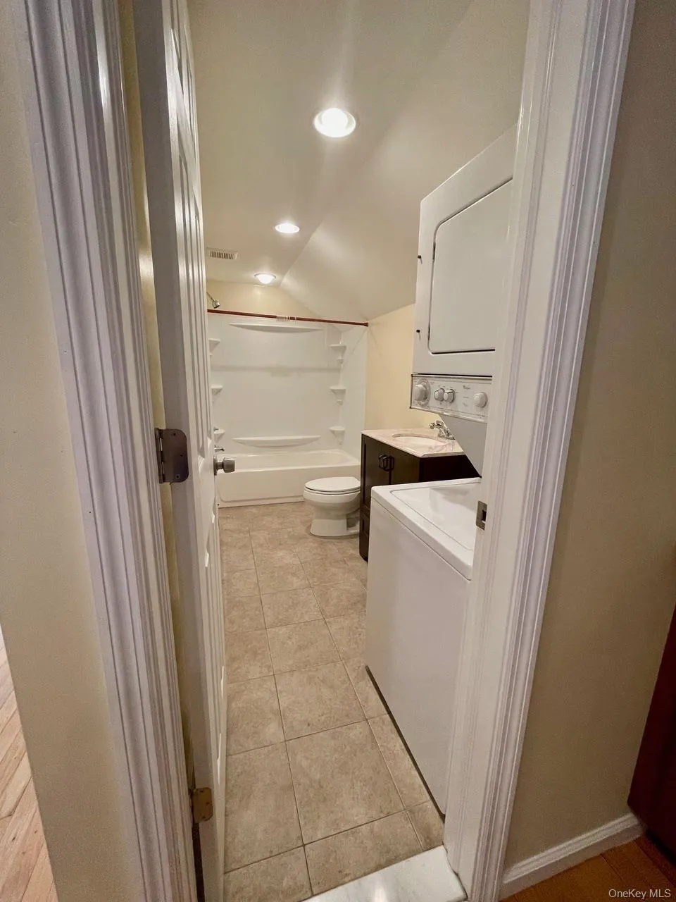 Full bath featuring lofted ceiling, vanity, shower / washtub combination, light tile patterned floors, and estacked washer and dryer Full bath featuring lofted ceiling, vanity, shower / washtub combination, light tile patterned floors, and estacked washer and dryer