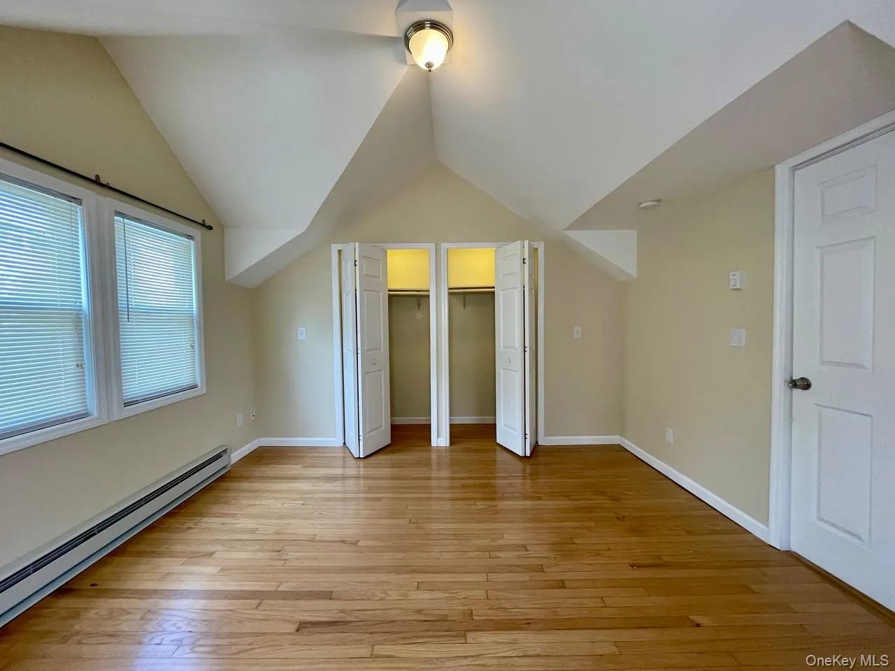 Unfurnished bedroom with a baseboard heating unit, multiple closets, light wood-style flooring, and lofted ceiling Unfurnished bedroom with a baseboard heating unit, multiple closets, light wood-style flooring, and lofted ceiling