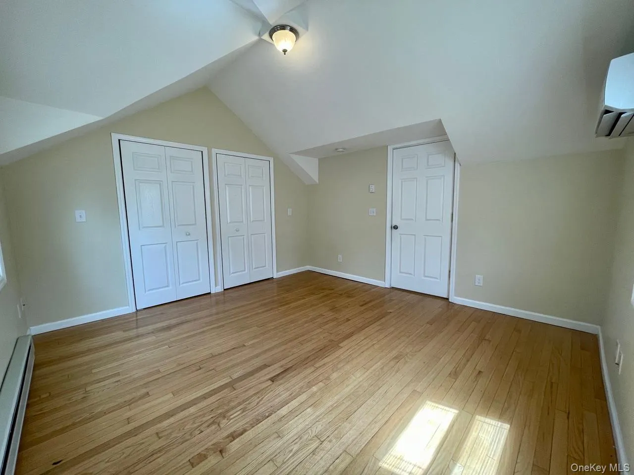 Additional living space featuring a baseboard heating unit, vaulted ceiling, light wood-style floors, and a wall mounted air conditioner Additional living space featuring a baseboard heating unit, vaulted ceiling, light wood-style floors, and a wall mounted air conditioner