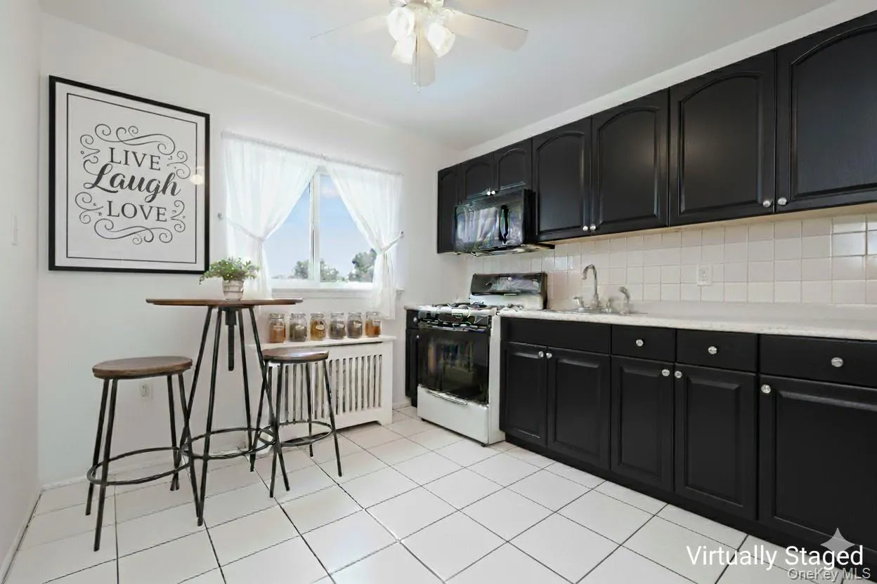 Kitchen featuring dark cabinets, white range with gas cooktop, tasteful backsplash, black microwave, and light tile patterned flooring Kitchen featuring dark cabinets, white range with gas cooktop, tasteful backsplash, black microwave, and light tile patterned flooring