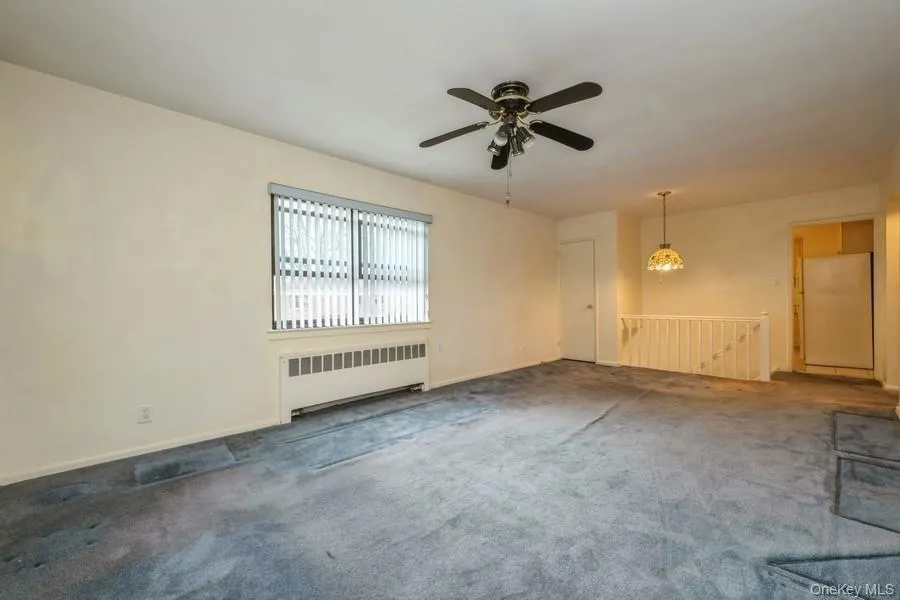 Unfurnished living room featuring radiator heating unit, carpet, and a ceiling fan Unfurnished living room featuring radiator heating unit, carpet, and a ceiling fan