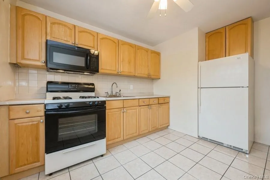 Kitchen with range with gas cooktop, freestanding refrigerator, black microwave, light countertops, and tasteful backsplash Kitchen with range with gas cooktop, freestanding refrigerator, black microwave, light countertops, and tasteful backsplash
